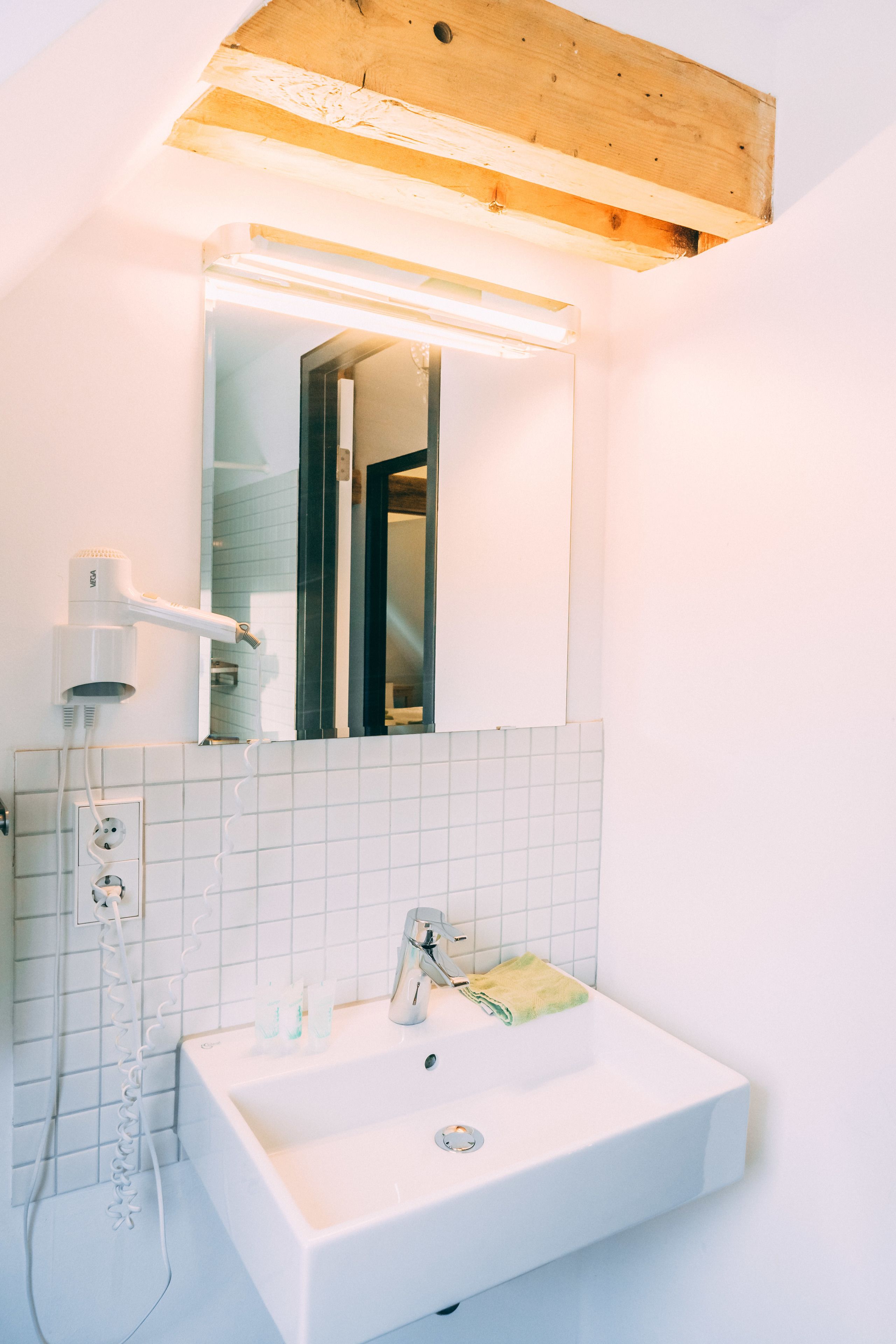 Ein Badezimmer mit einem weißen Waschbecken, einem Spiegel und einem Föhn.