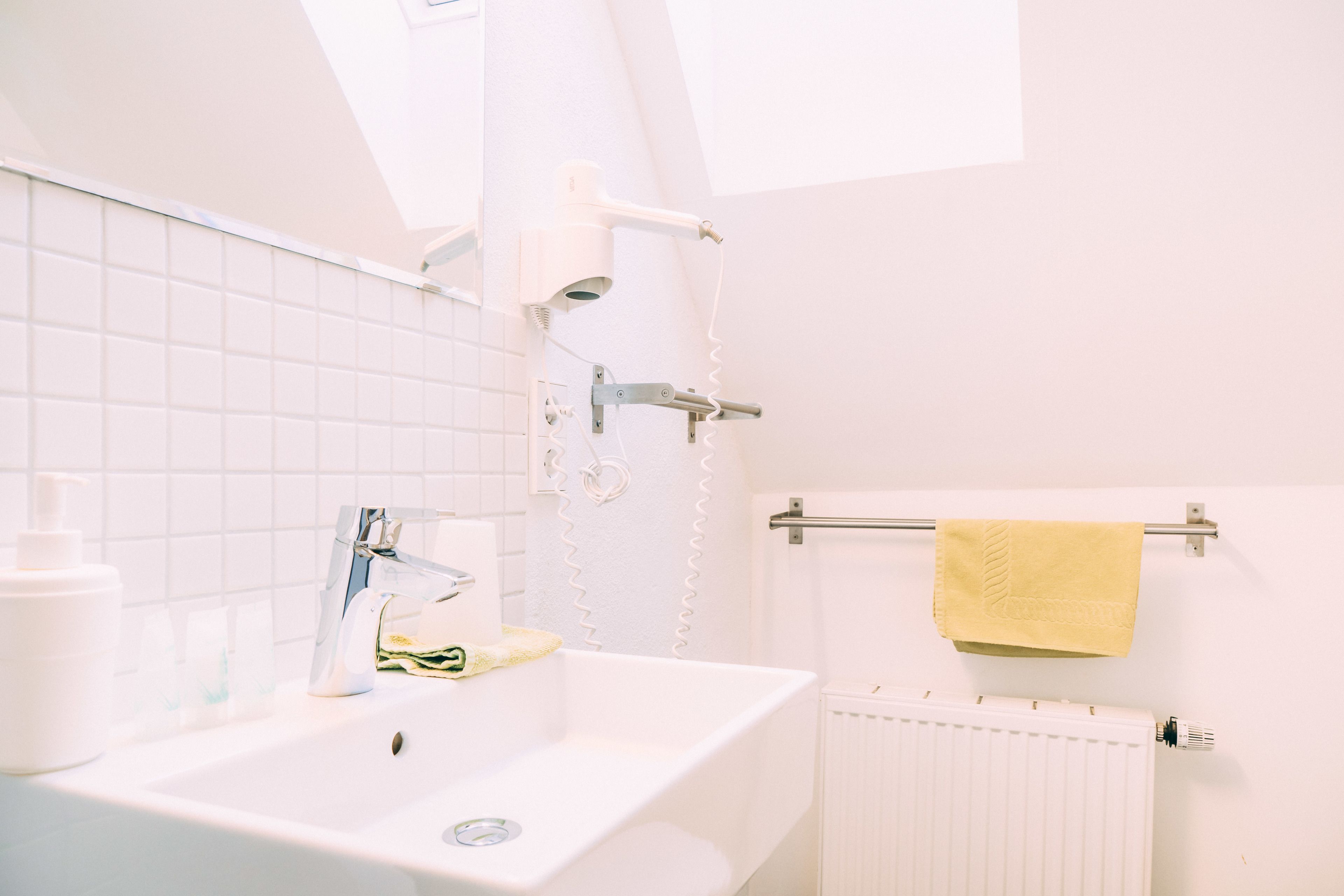 A bathroom with a white sink, a towel rack with a yellow towel, and a white radiator.