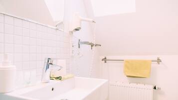 Une salle de bain avec un lavabo blanc, un porte-serviettes sur lequel est posée une serviette jaune, et un radiateur blanc.