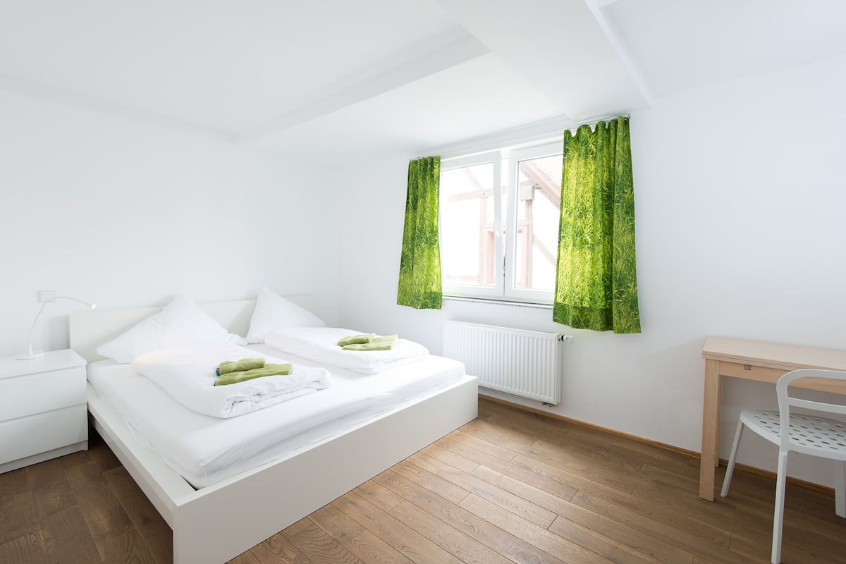Ein modernes Schlafzimmer mit Bett, Nachttischen, einem Schreibtisch und einem Fenster mit Vorhängen.