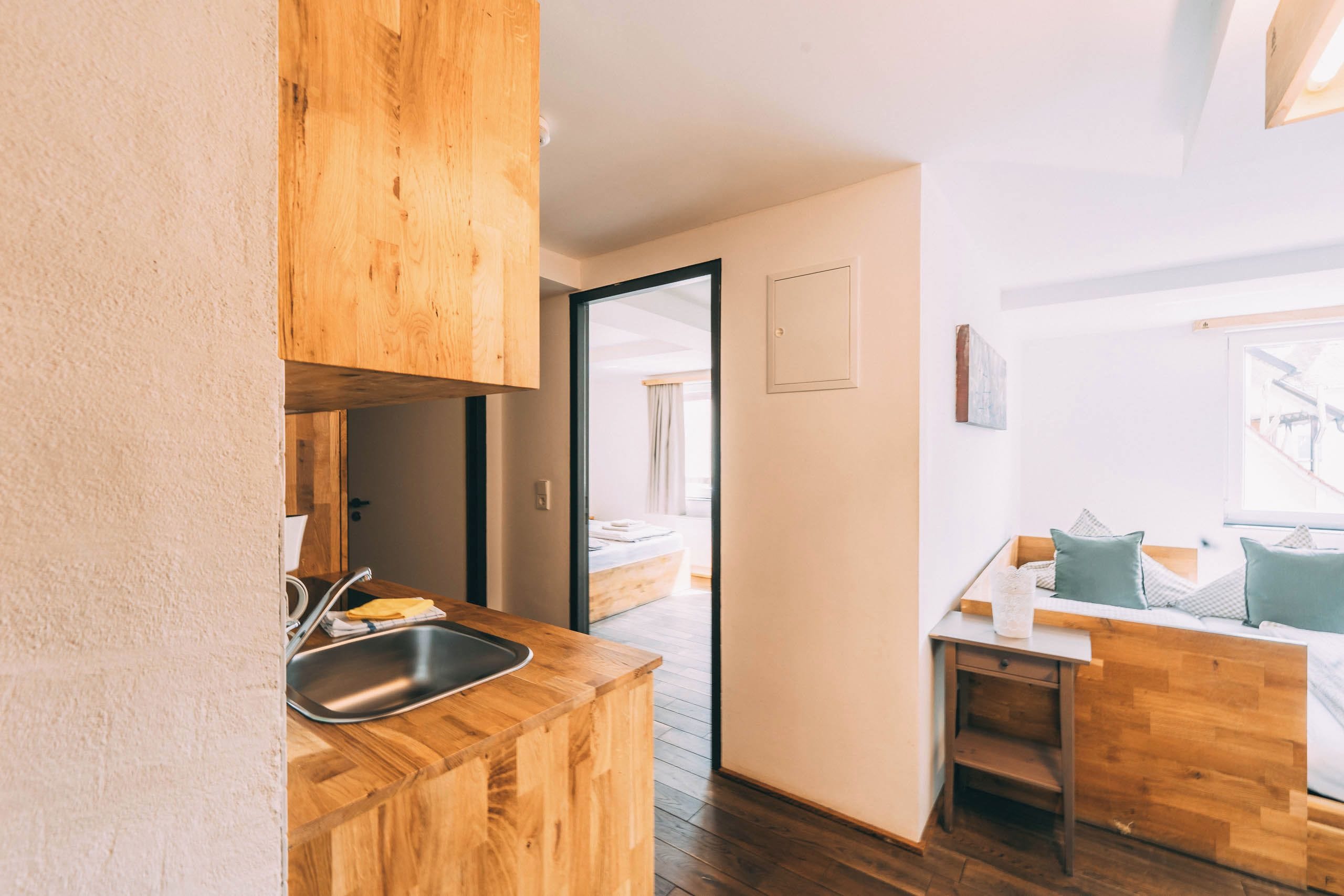 A compact kitchen with a wooden countertop, a sink, and a door leading to a bedroom.