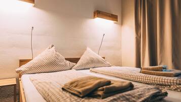 A hotel room with a bed, two pillows, a blanket, a wooden headboard, a wall-mounted light, and a window with curtains.
