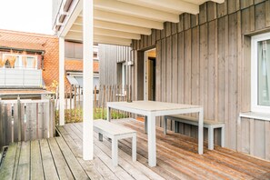 A wooden deck with a white table and bench, a wooden wall, and a window. - Stadthaus Gut Hügle (Ravensburg)