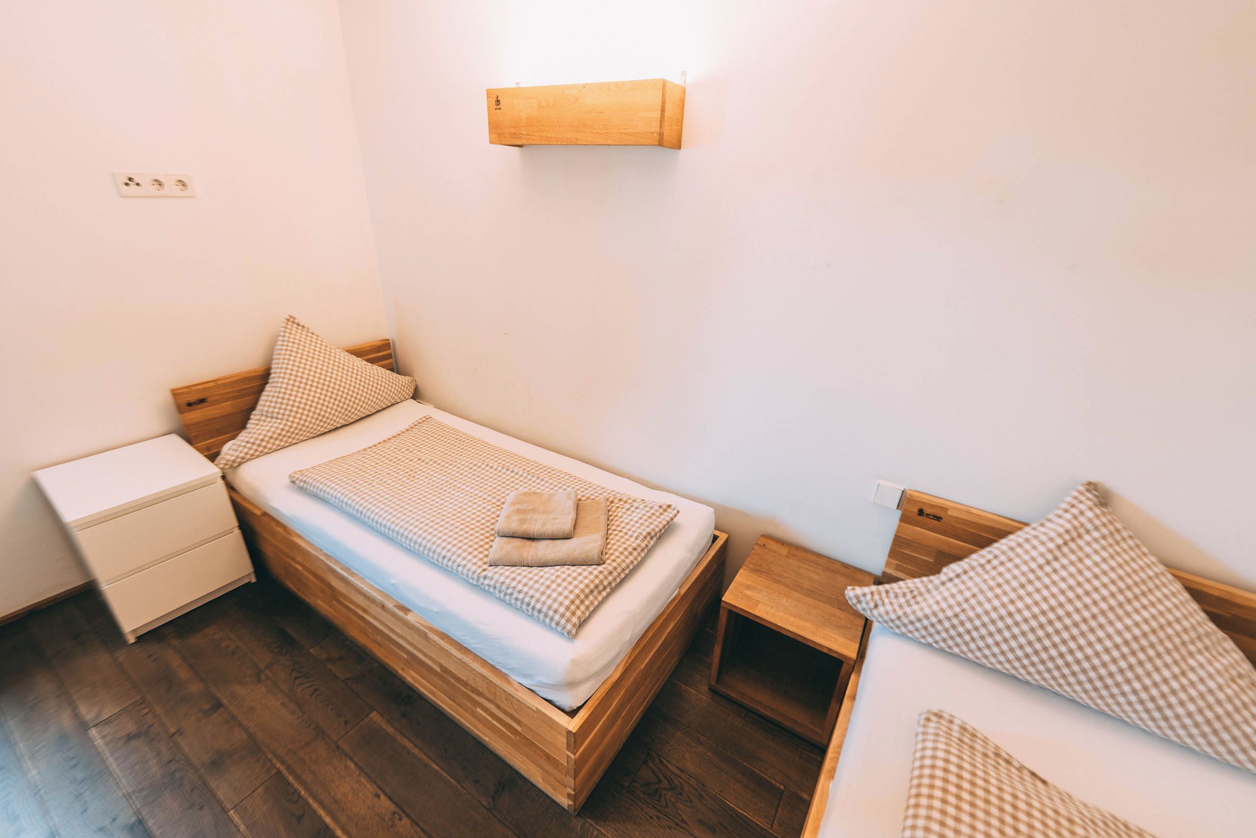 Un dormitorio pequeño y ordenado con una cama individual, una mesita de noche, una lámpara de pared y una luz empotrada.