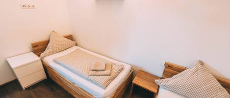 Un dormitorio pequeño y ordenado con una cama individual, una mesita de noche, una lámpara de pared y una luz empotrada.
