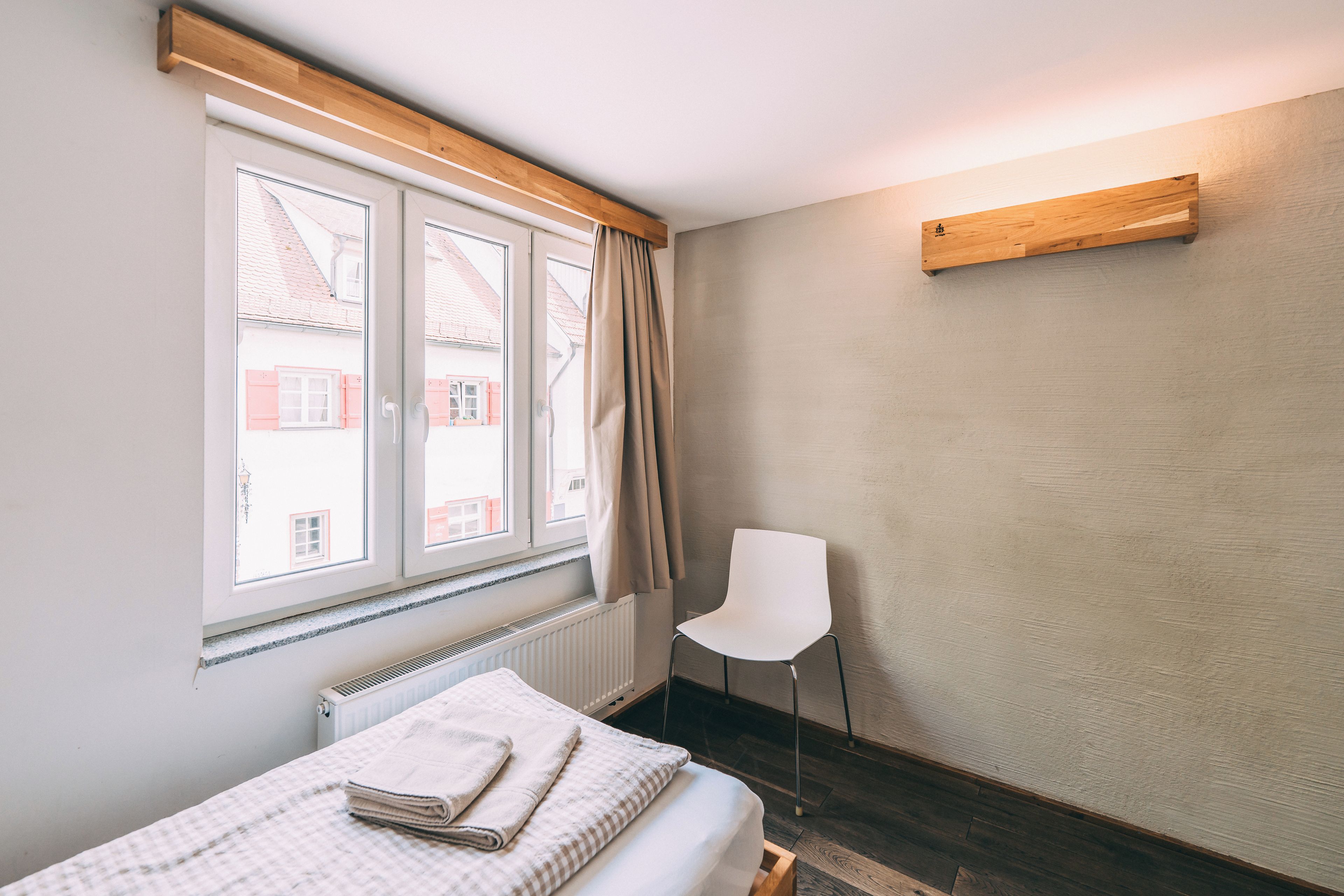 Quarto com cama, cadeira, janela com cortinas e radiador.