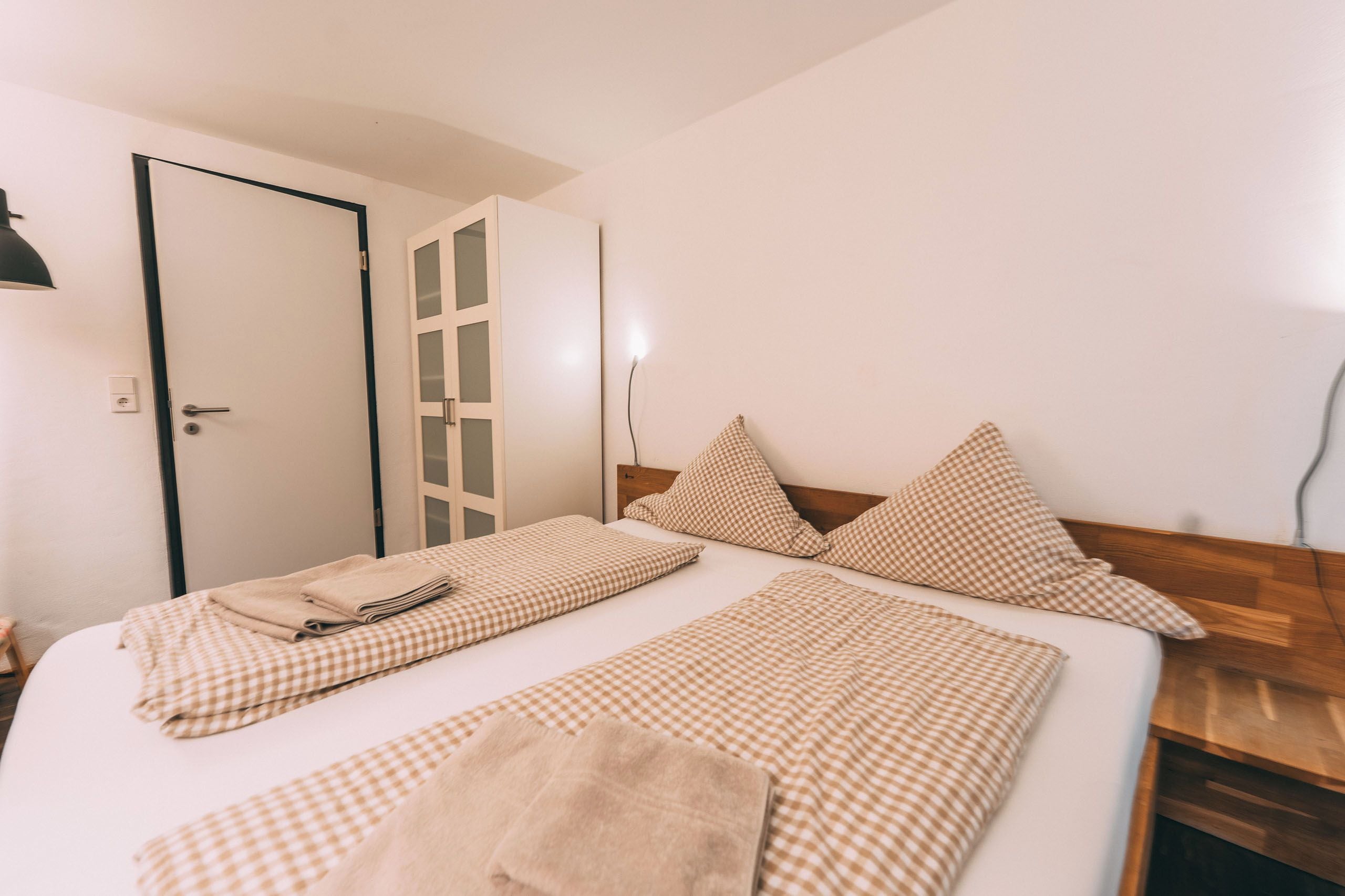 Una cama individual con ropa de cama a cuadros, un cabecero de madera y una mesita de noche con una lámpara.