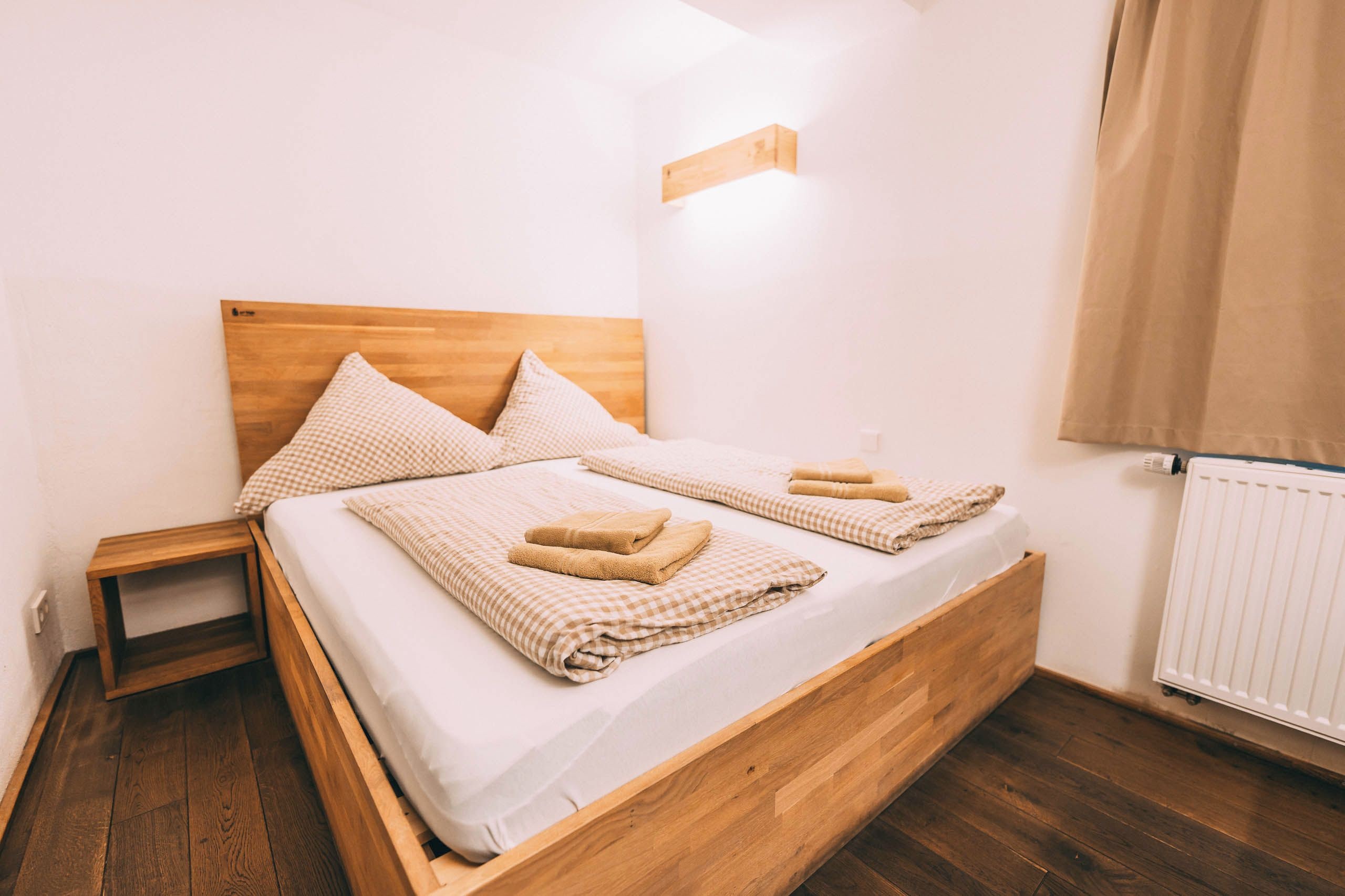 A double bed with a wooden headboard, two pillows, a bedside table, and a radiator.