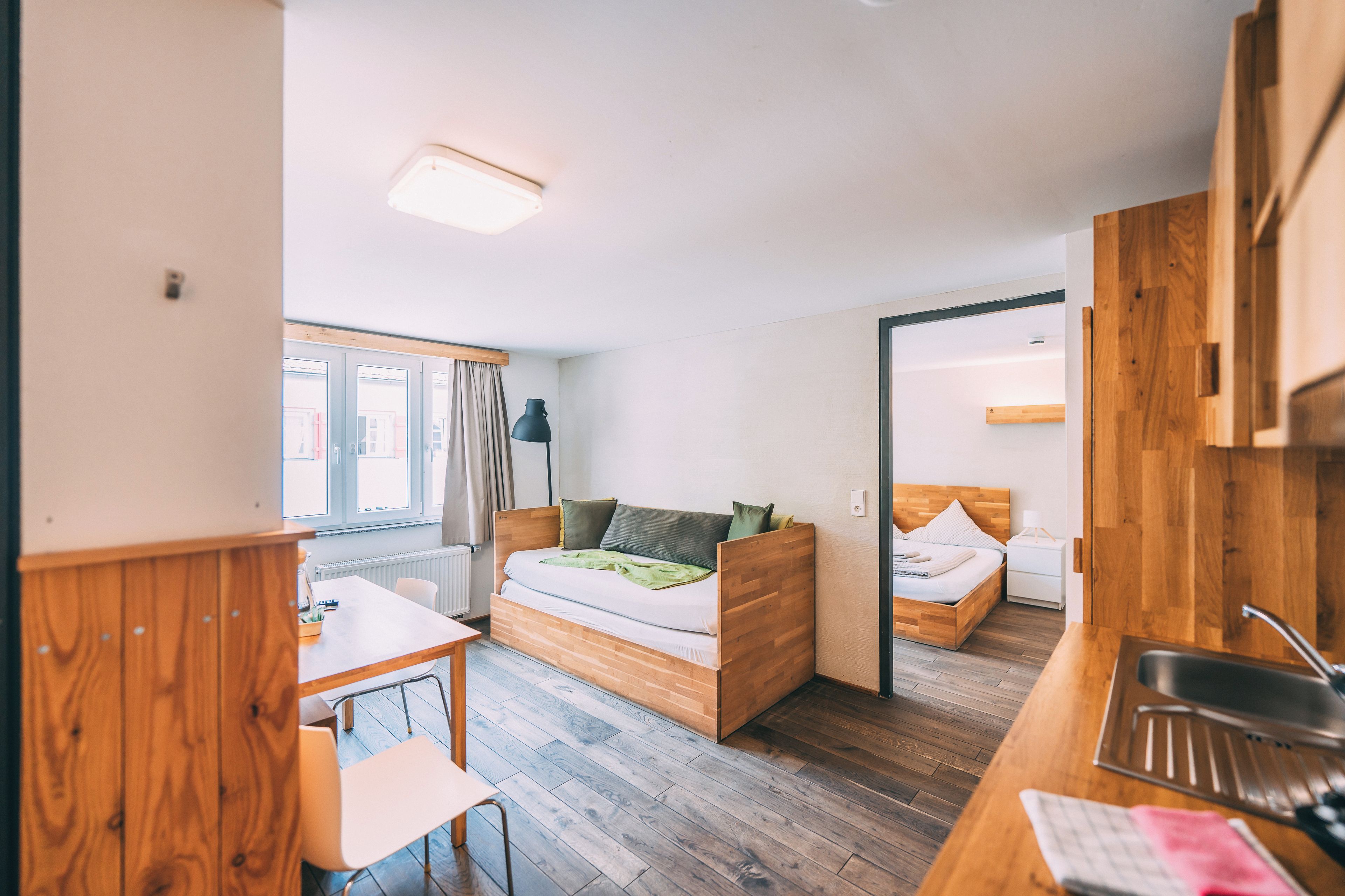 A compact room with a bed, a small table, and a kitchenette area.