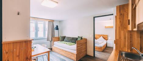A compact room with a bed, a small table, and a kitchenette area.