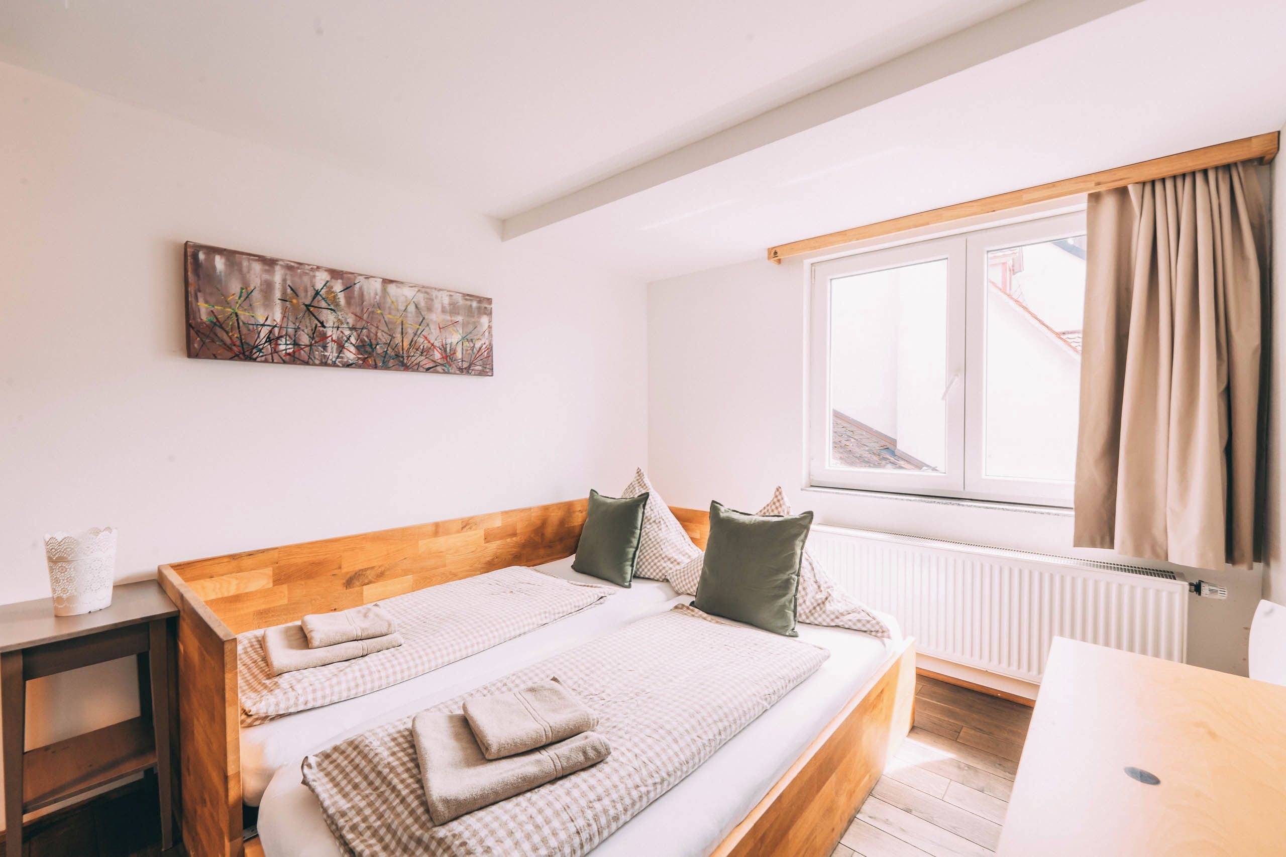 A bedroom with a wooden headboard, a bed with checkered bedding, a radiator, and a window with curtains.