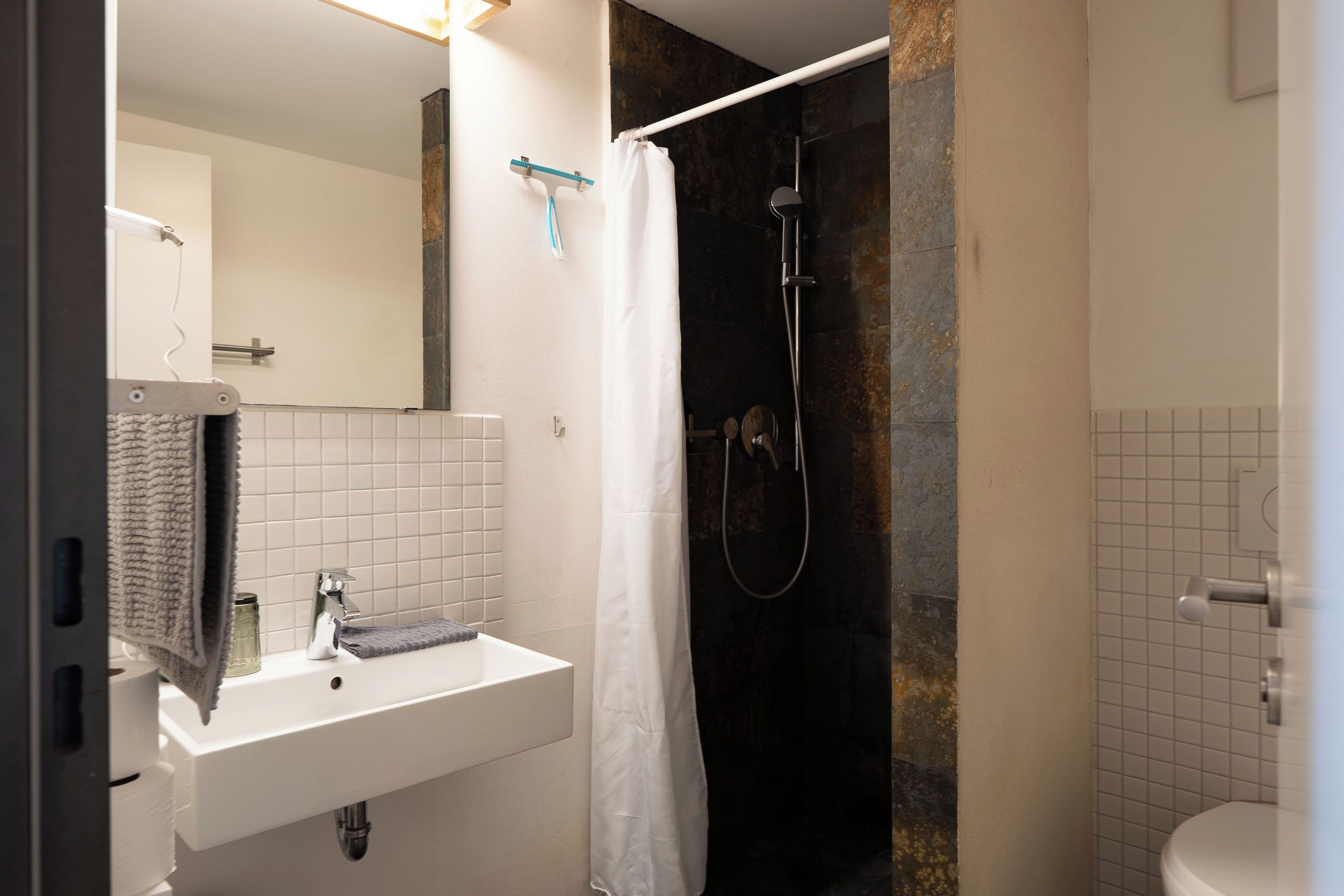 A bathroom with a white sink, a mirror, a shower with a curtain, and a toilet.
