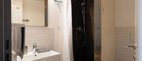 A bathroom with a white sink, a mirror, a shower with a curtain, and a toilet.