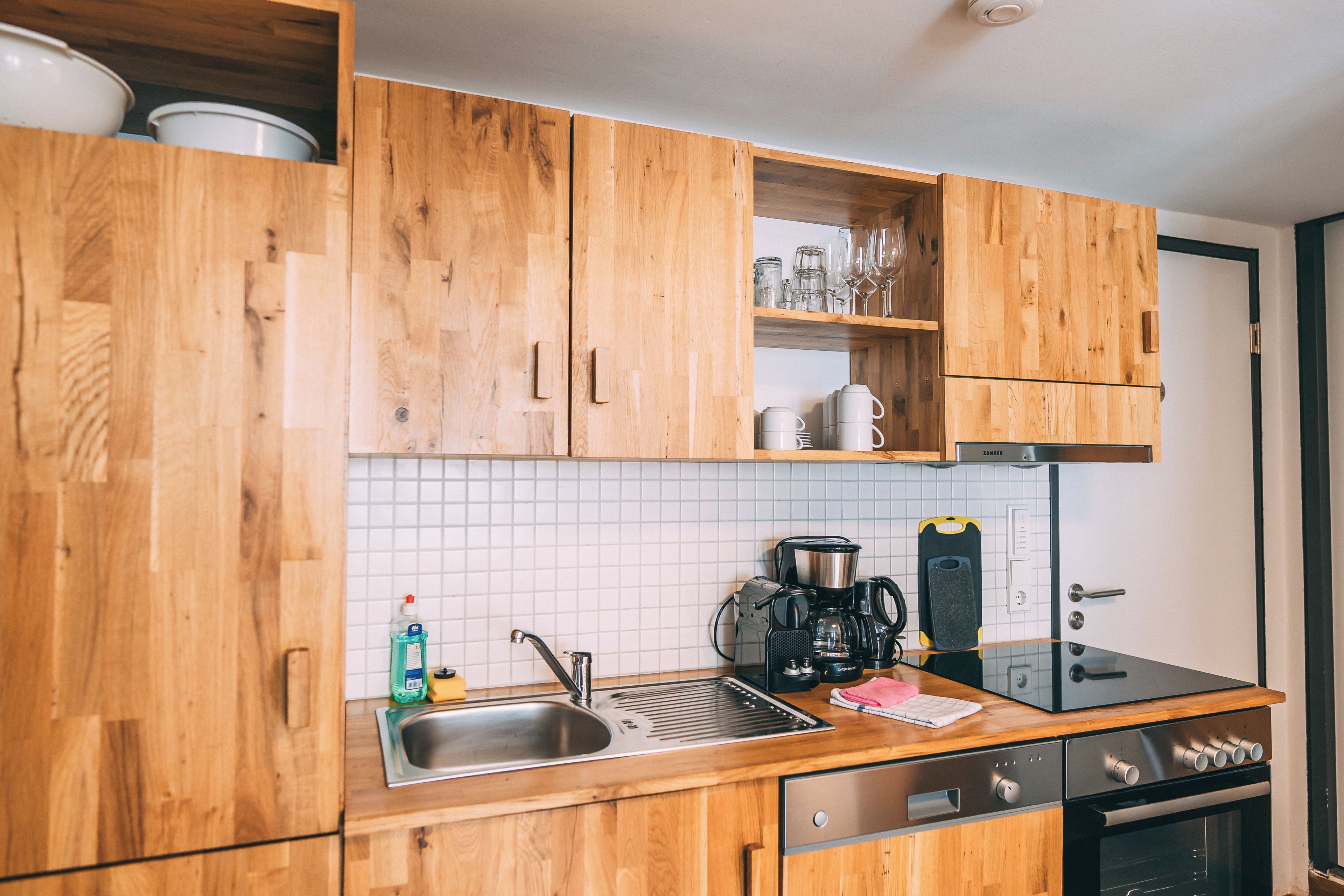Una cocina con armarios de madera, un lavamanos de acero inoxidable, una cafetera y un microondas.