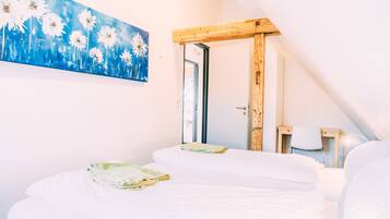 A bedroom with two beds, a wooden ceiling beam, a painting of daisies, and a view of the outdoors.