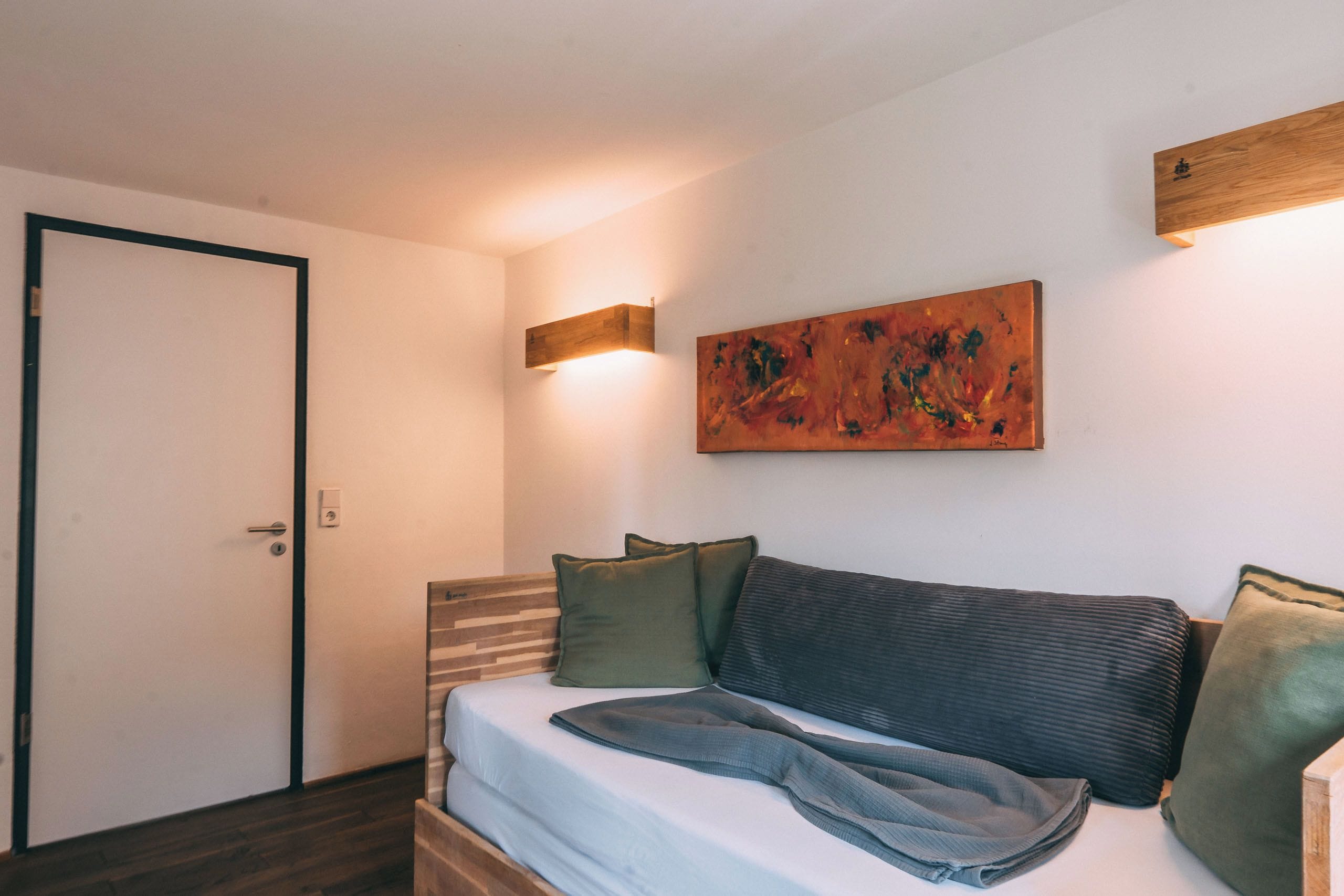 A bedroom with a bed, a painting, and a wall-mounted light fixture.
