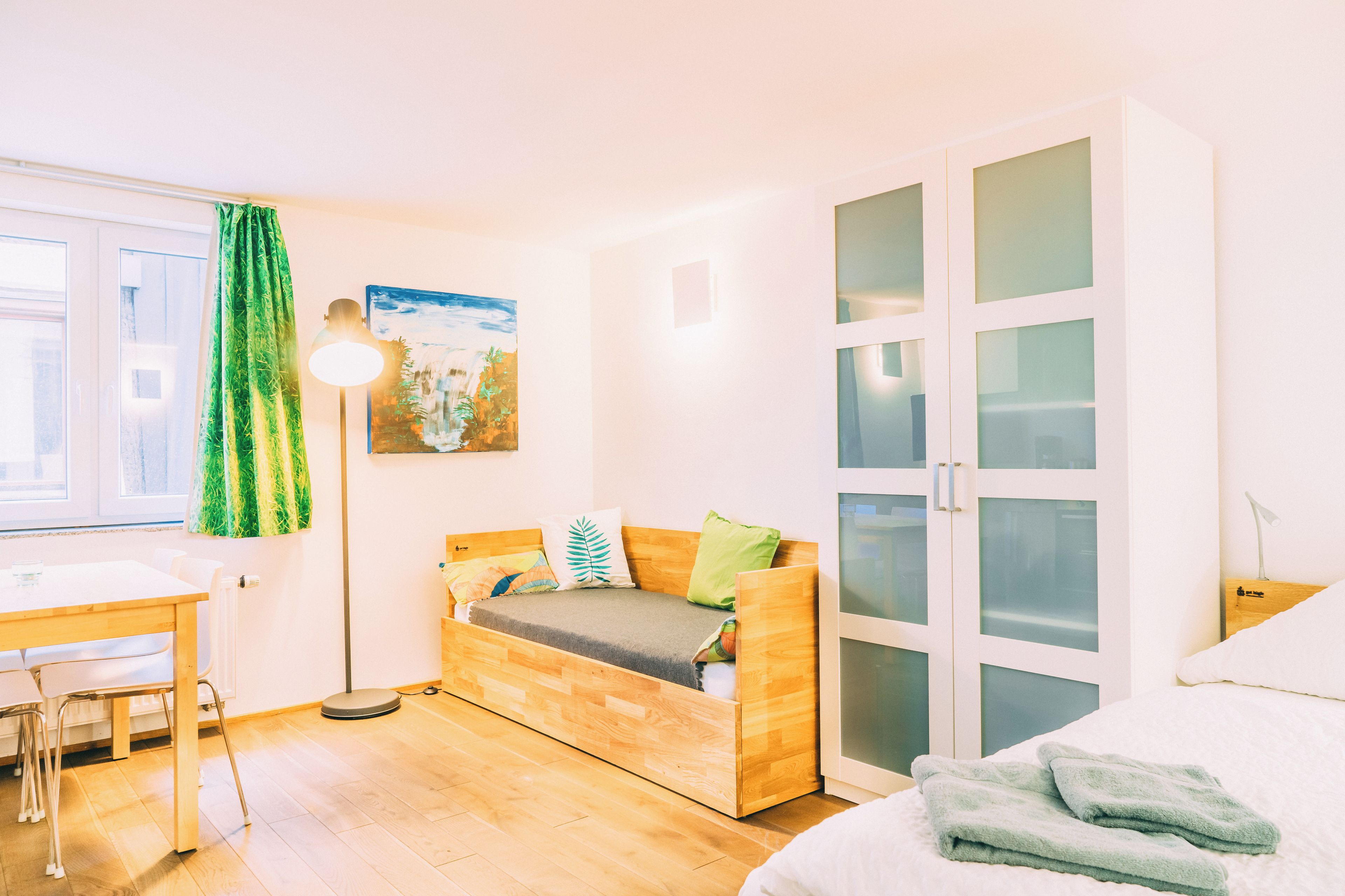 A room with a bed, a desk, a chair, a wardrobe, and a painting on the wall.