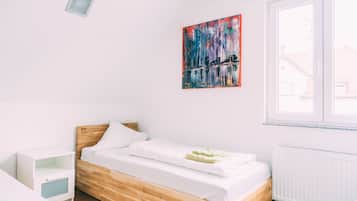 Een moderne slaapkamer met een houten bed, witte beddengoed, een klein nachtkastje en een kleurrijk abstract schilderij aan de muur.