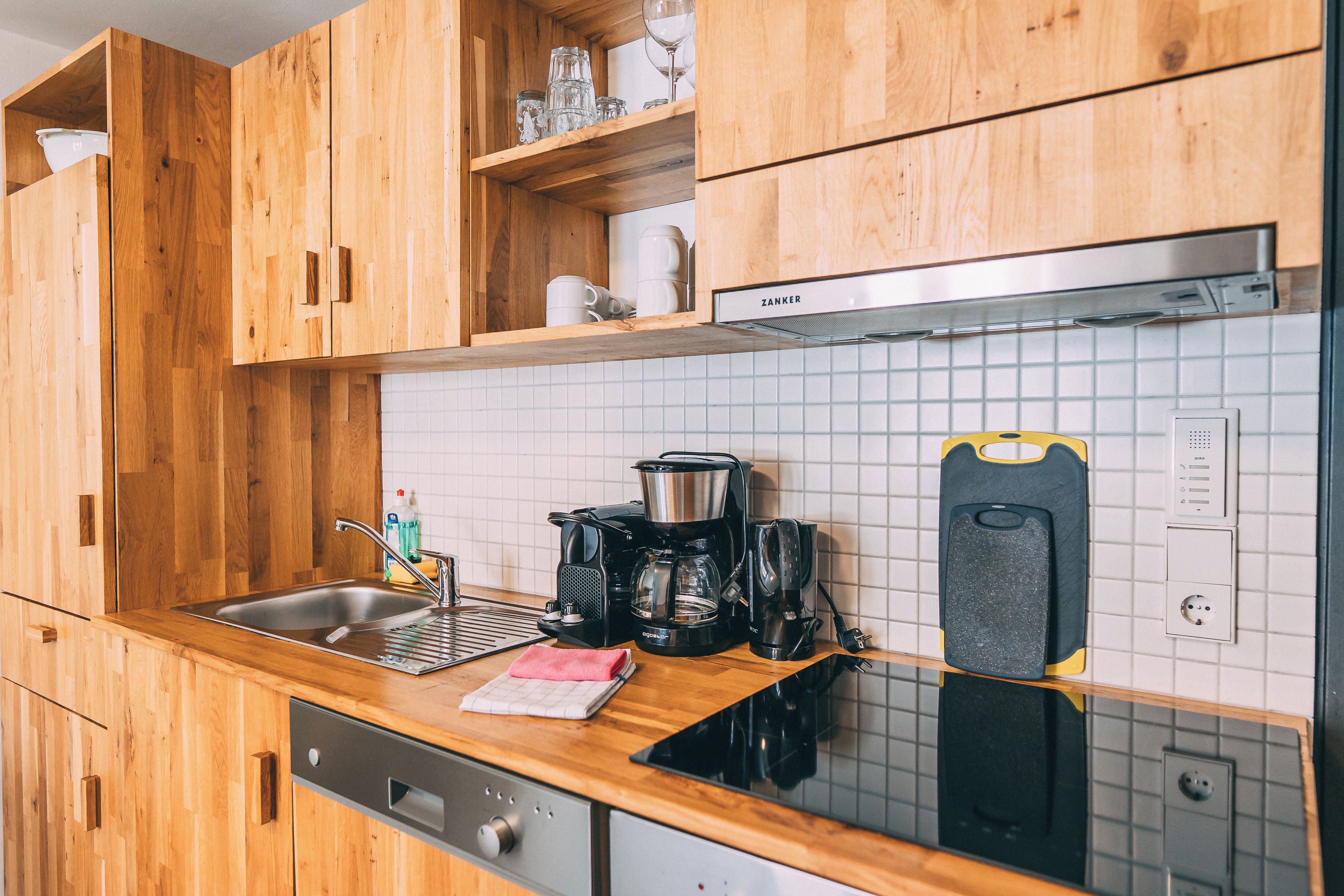 A modern kitchen with wooden cabinets, a stainless steel sink, a coffee maker, and a kettle.