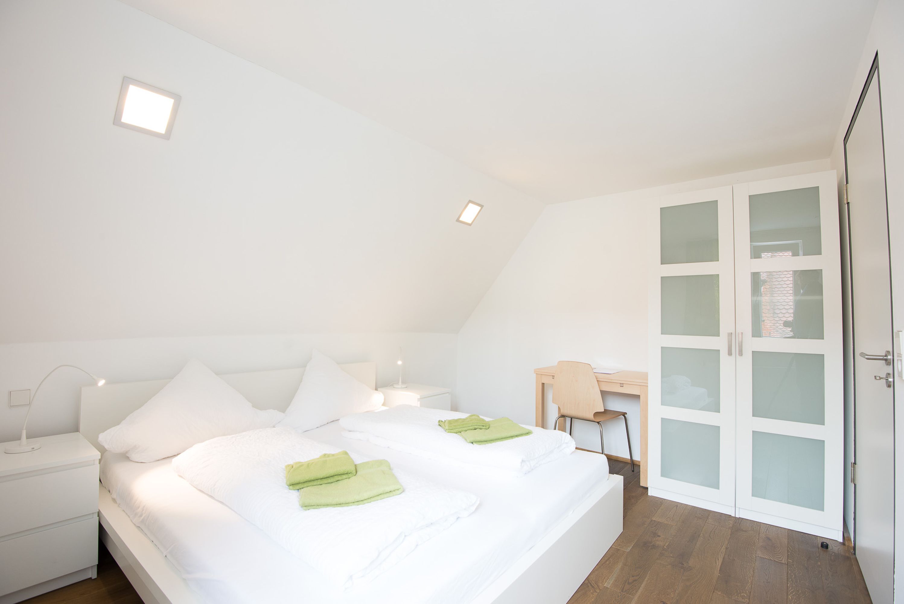 A bedroom with a bed, bedside tables, a desk, and a wardrobe.