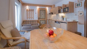 Ein gemütliches Wohnzimmer mit einer Couch, einem Holzesstisch mit Obstschale und einer Küchenzeile mit Holzschränken und Geräten.