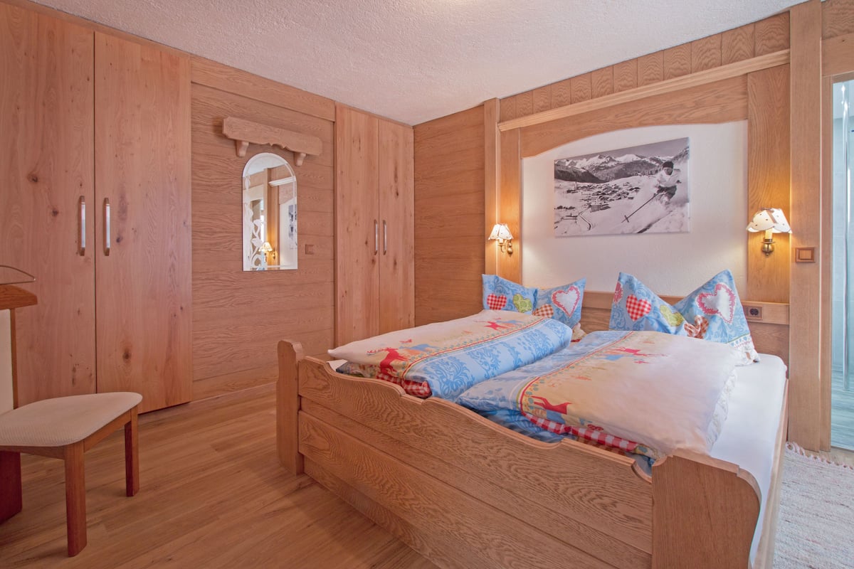 A wooden bedroom with a bed, a chair, and a mirror.