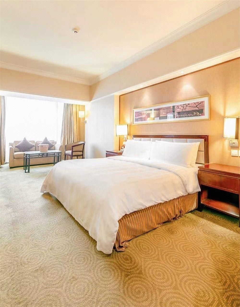 A hotel room with a large bed, a bedside table, a chair, a sofa, and a window with curtains.