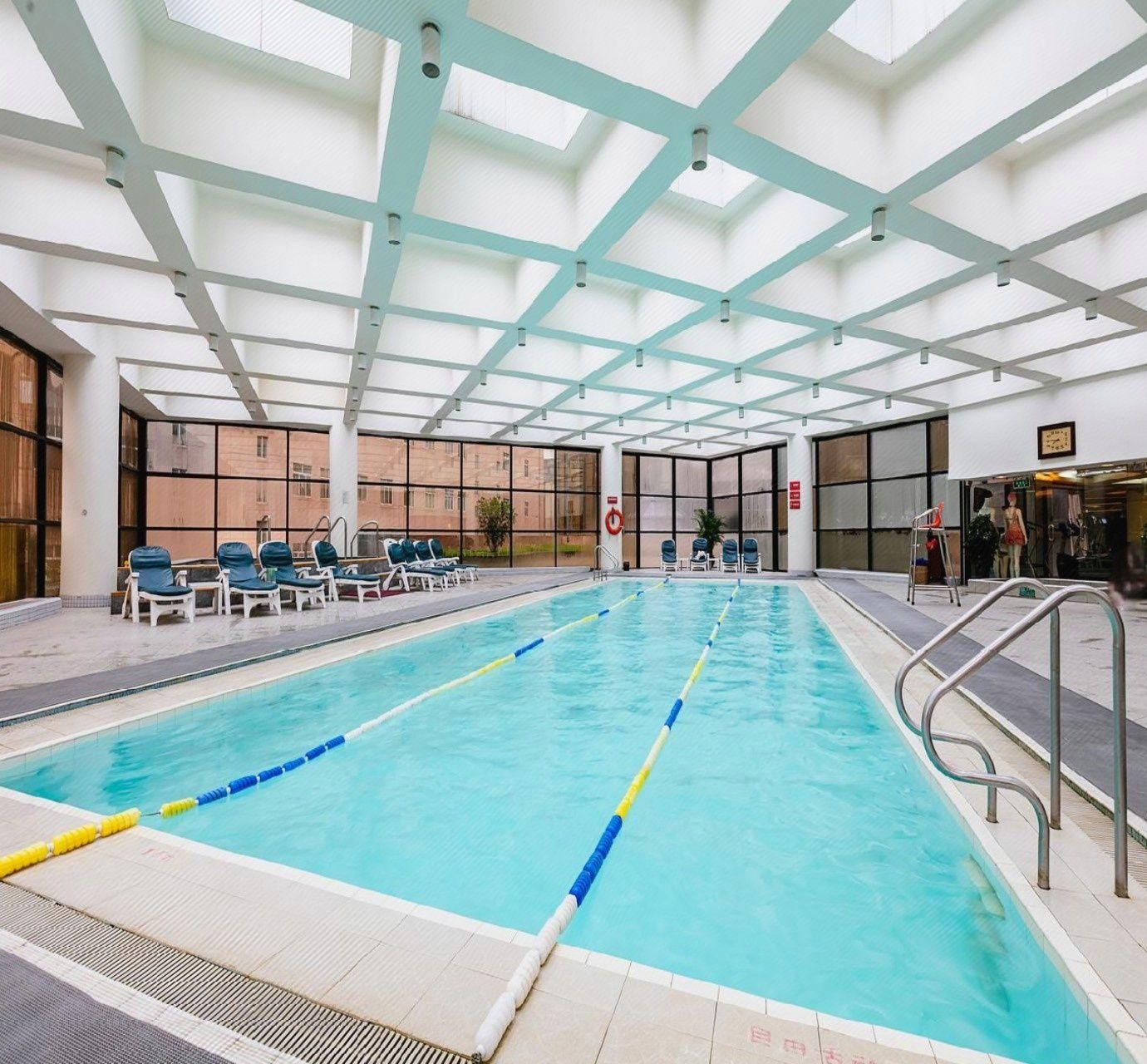 An indoor swimming pool with clear lanes, a sunroof, and lounge chairs.