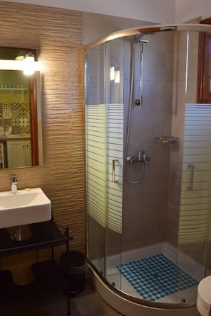 Un baño moderno con ducha de vidrio, un lavabo con espejo y un suelo estampado.