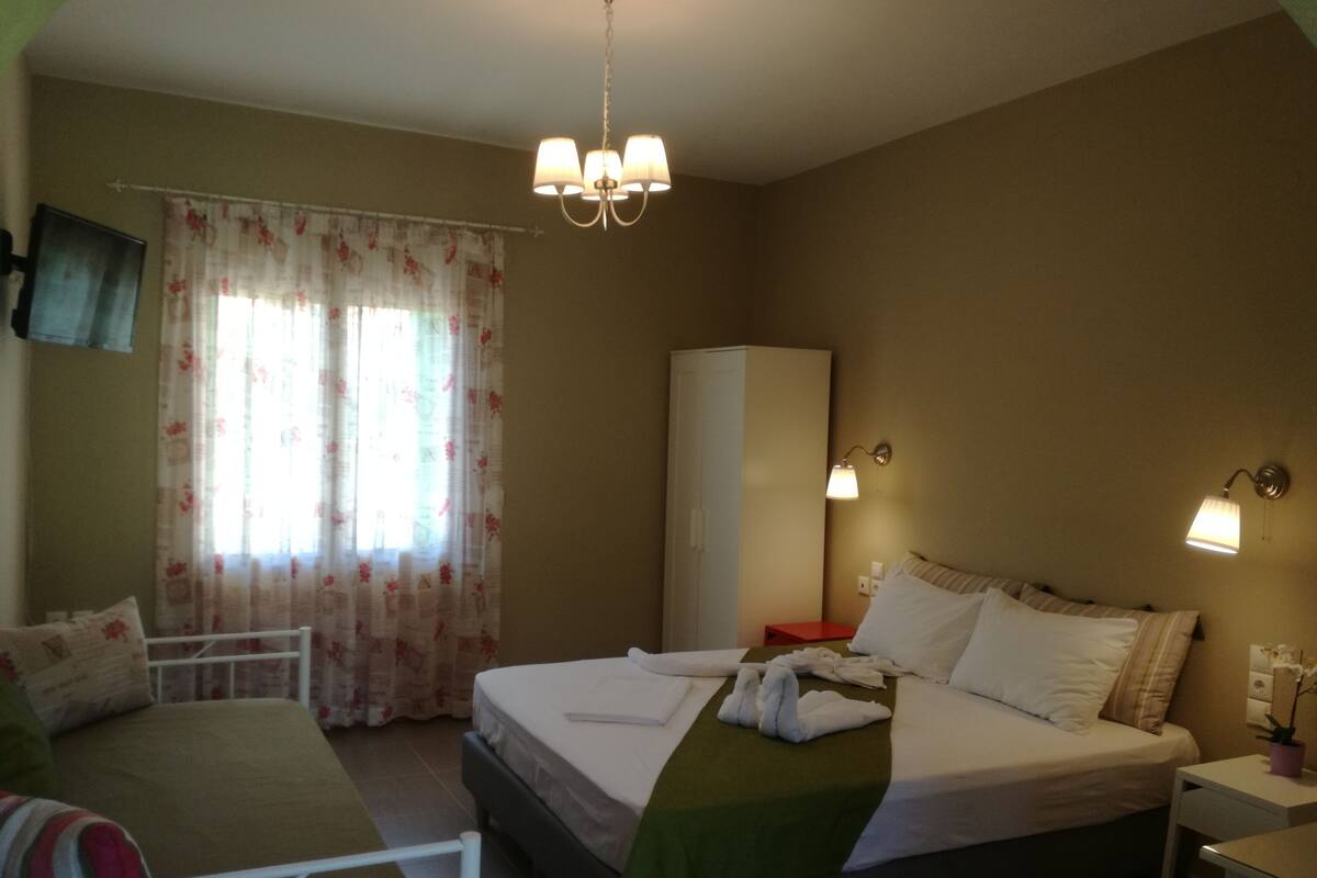 A hotel room with a bed, bedside tables, a wardrobe, a television, and a chandelier.