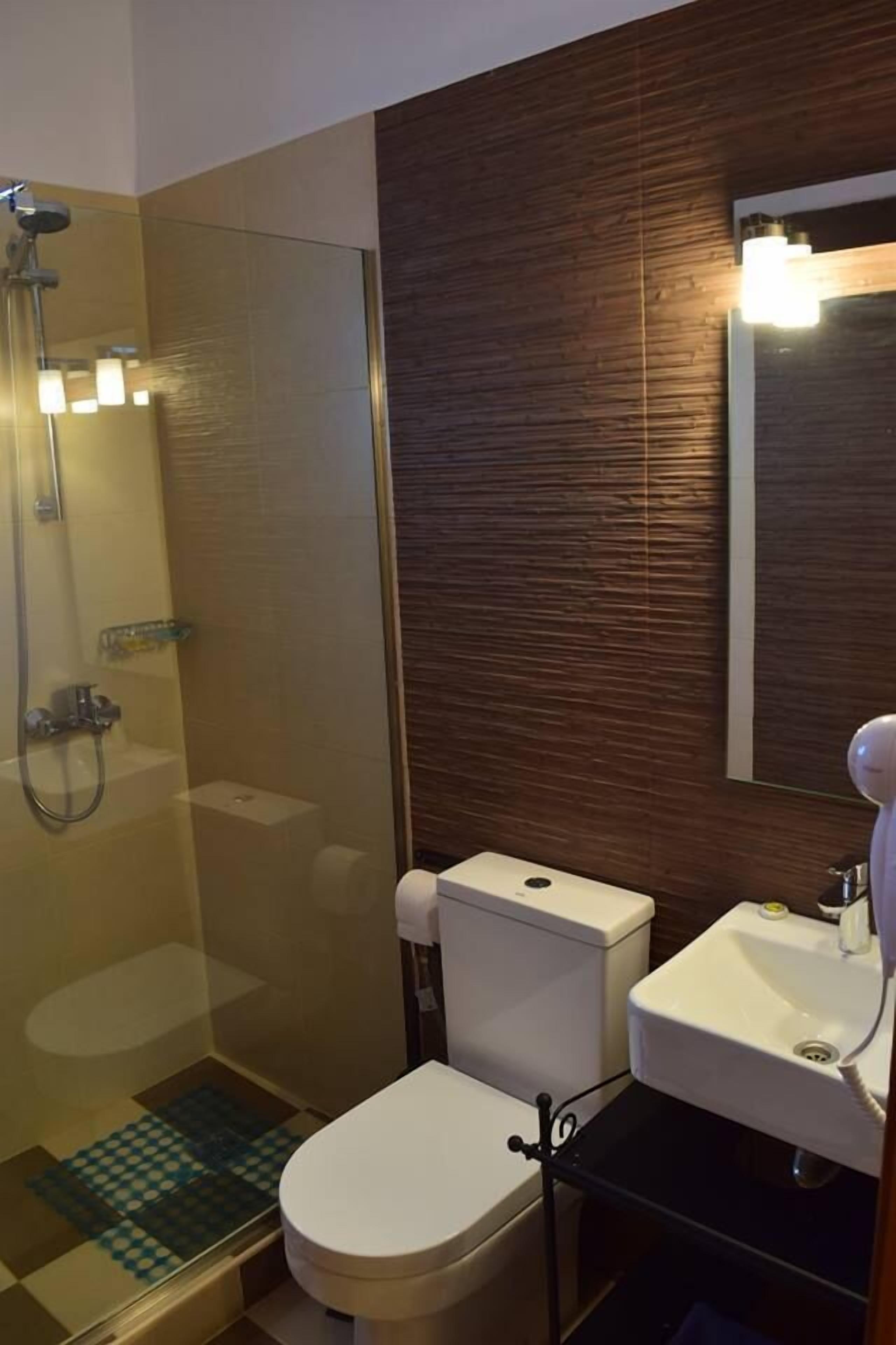 A bathroom with a glass-enclosed shower, a white toilet, and a sink with a mirror above it.