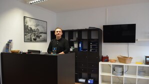 Une salle d’attente avec un bureau noir, un téléviseur à écran plat, une bibliothèque et un tableau encadré au mur.