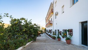 A narrow alleyway with a white building on one side, potted plants, and a bench. - Hostal Vista a la Sierra (Valle de Abdalagis)