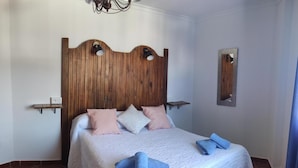 A bedroom with a wooden headboard, a bed with white bedding, two pillows, and a blue towel. - Hostal Vista a la Sierra (Valle de Abdalagis)