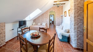 A cozy loft bedroom with a sloped ceiling, a brick wall, a wooden door, and a small dining area with a table and chairs. - Hostal Vista a la Sierra (Valle de Abdalagis)