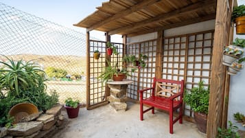 A covered outdoor seating area with a wooden bench, potted plants, and a stone table.