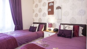 Une chambre avec deux lits, une table de chevet, une lampe et un mur décoré de motifs d’arbres.
