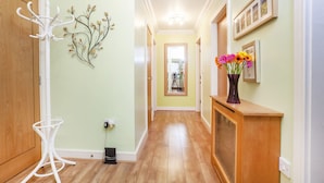 Un couloir avec un plancher en bois, un porte-manteau blanc, une plante fixée au mur et un vase rempli de fleurs.