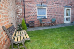 A brick building with a bench, a small table, and two chairs in the yard.