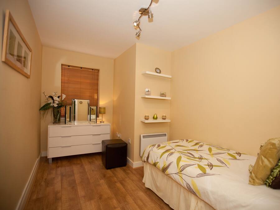 Een slaapkamer met een bed, een dressoir, een spiegel en een plank met decoratieve objecten.