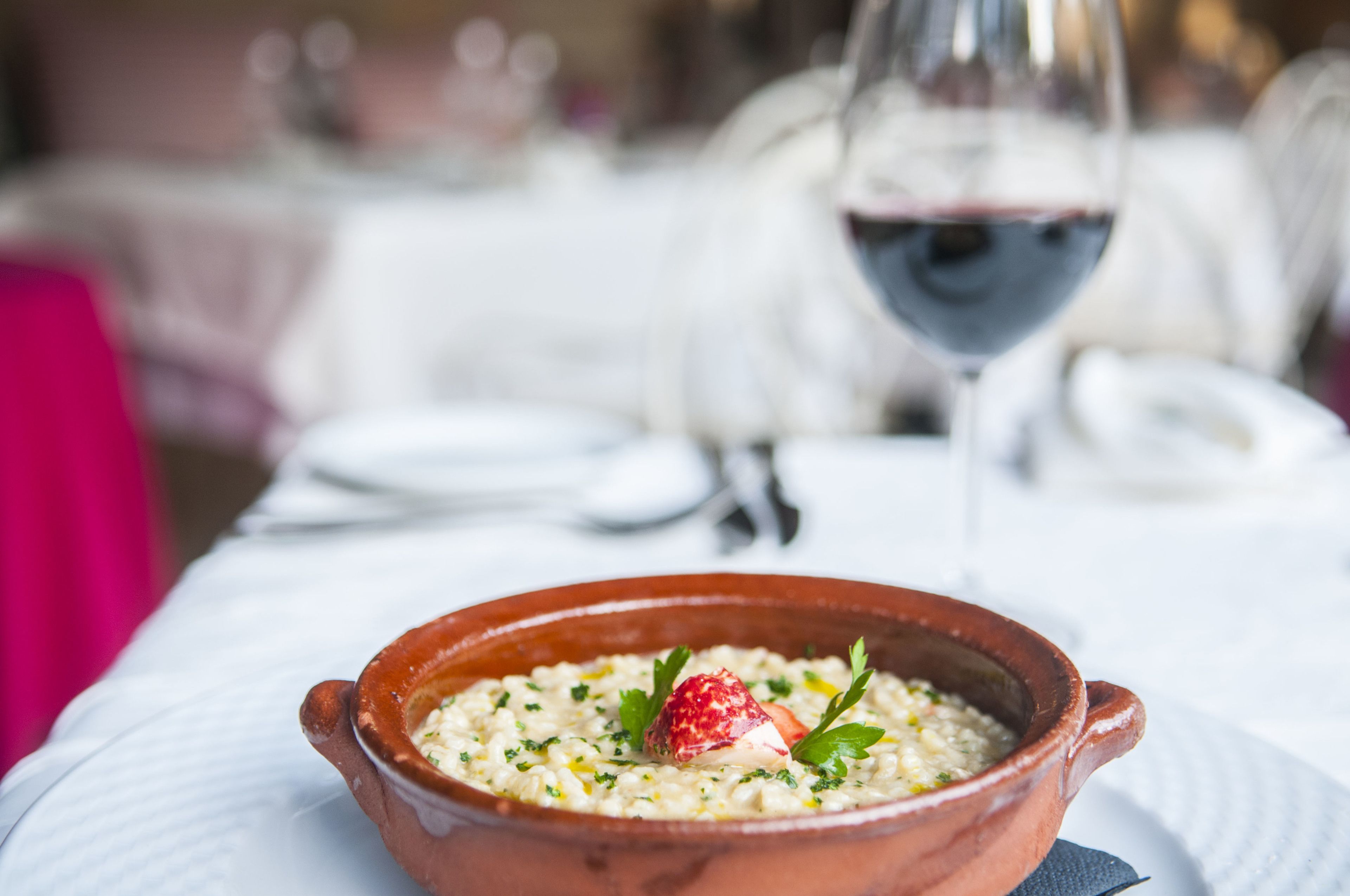 A bowl of food on a table with a wine glass in the background.