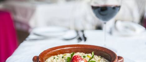A bowl of food on a table with a wine glass in the background.