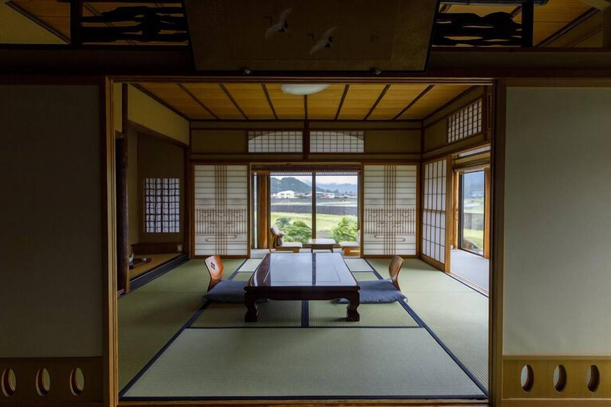 Una habitación tradicional japonesa con suelo de tatami, puertas correderas y vistas a un paisaje.