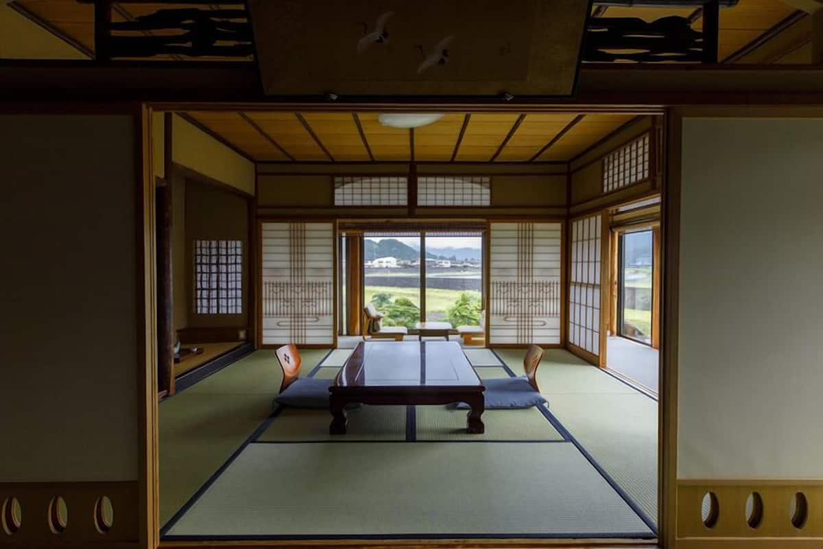 A traditional Japanese room with tatami flooring, sliding doors, and a view of a landscape.