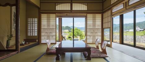 A traditional Japanese room with tatami flooring, a low wooden table, and sliding doors with a view of a mountainous landscape.