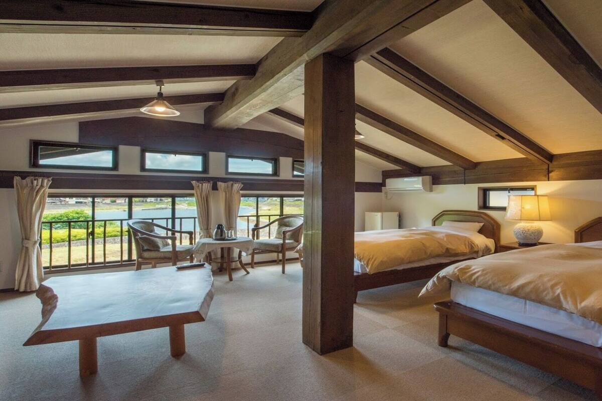 Una habitación con dos camas, una mesa, sillas y amplios ventanales con vistas panorámicas.