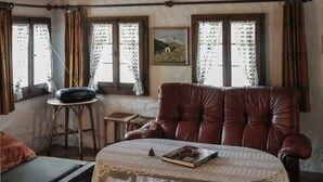 Um quarto aconchegante com uma poltrona de couro, uma mesinha com um livro, um rádio e uma janela com cortinas.