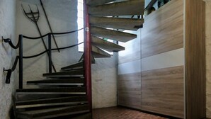 Escadaria em espiral com guarda-corrimãos de metal e um pilar de suporte vermelho, que dá acesso a um espaço com paredes de painel de madeira e piso de azulejos.