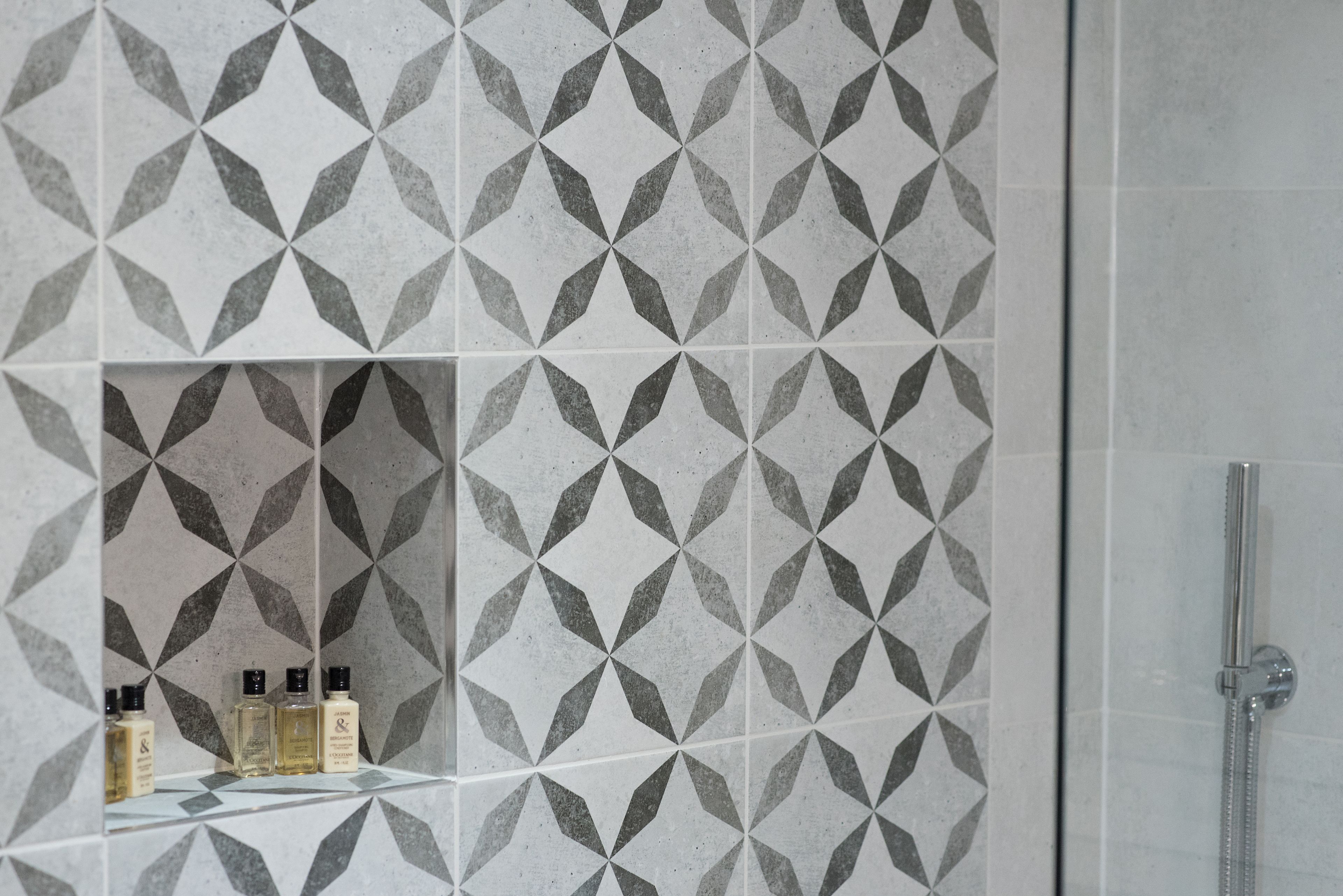 A bathroom with a geometric tile pattern, a shower, and a shelf with toiletries.