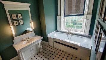 A bathroom with a white vanity, a large bathtub, and a window with a view of greenery.